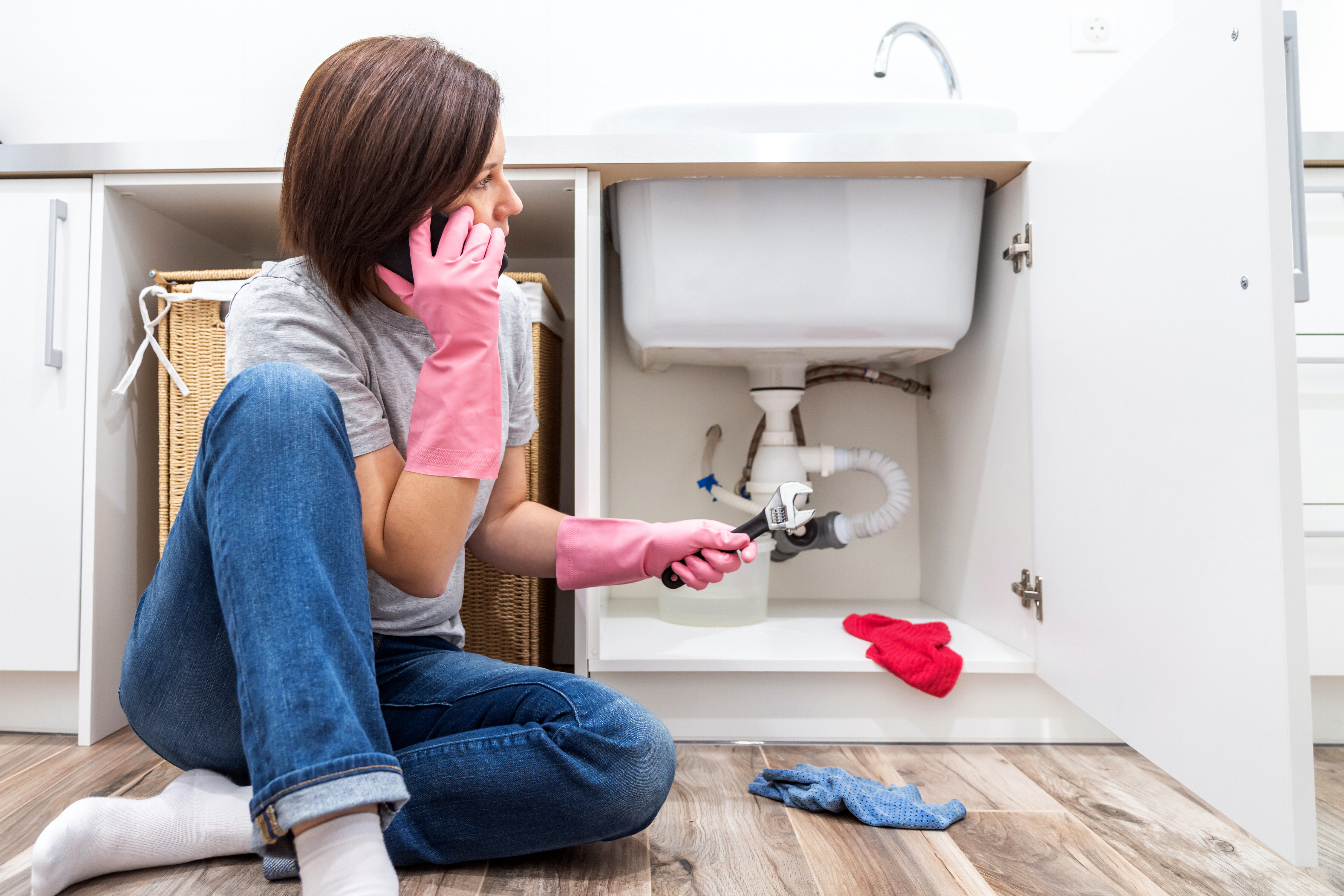 woman talking on the phone while sitting on the floor and dealing with plumbing emergency